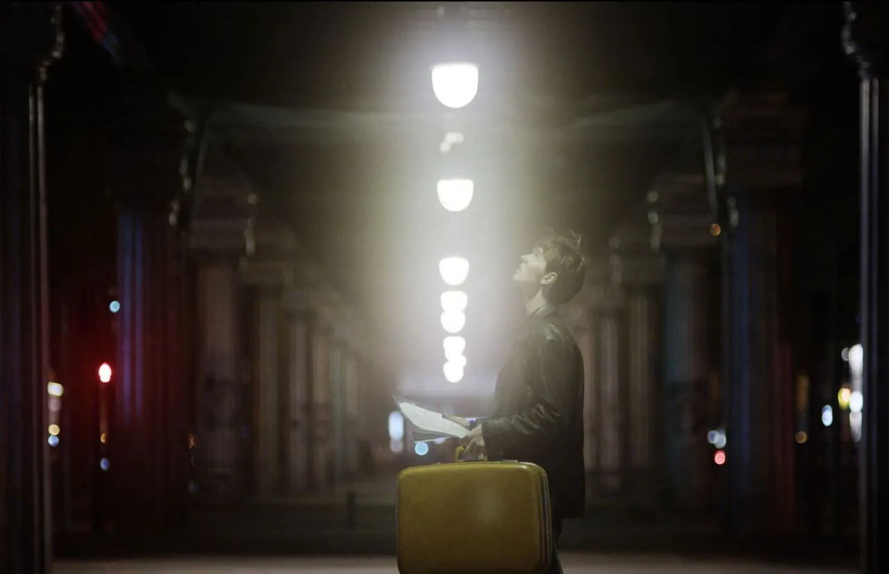 Person sitting with a yellow suitcase beneath a row of streetlights.