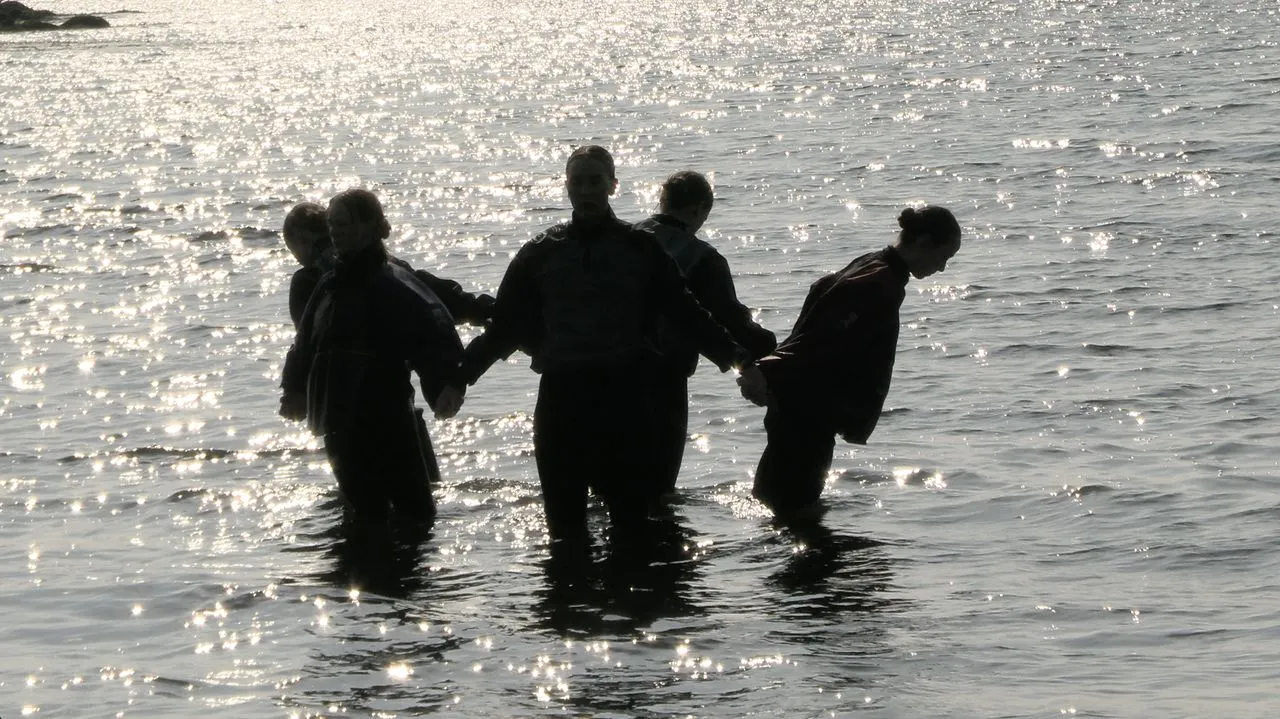 Three people holding hands while standing in sunlit water.