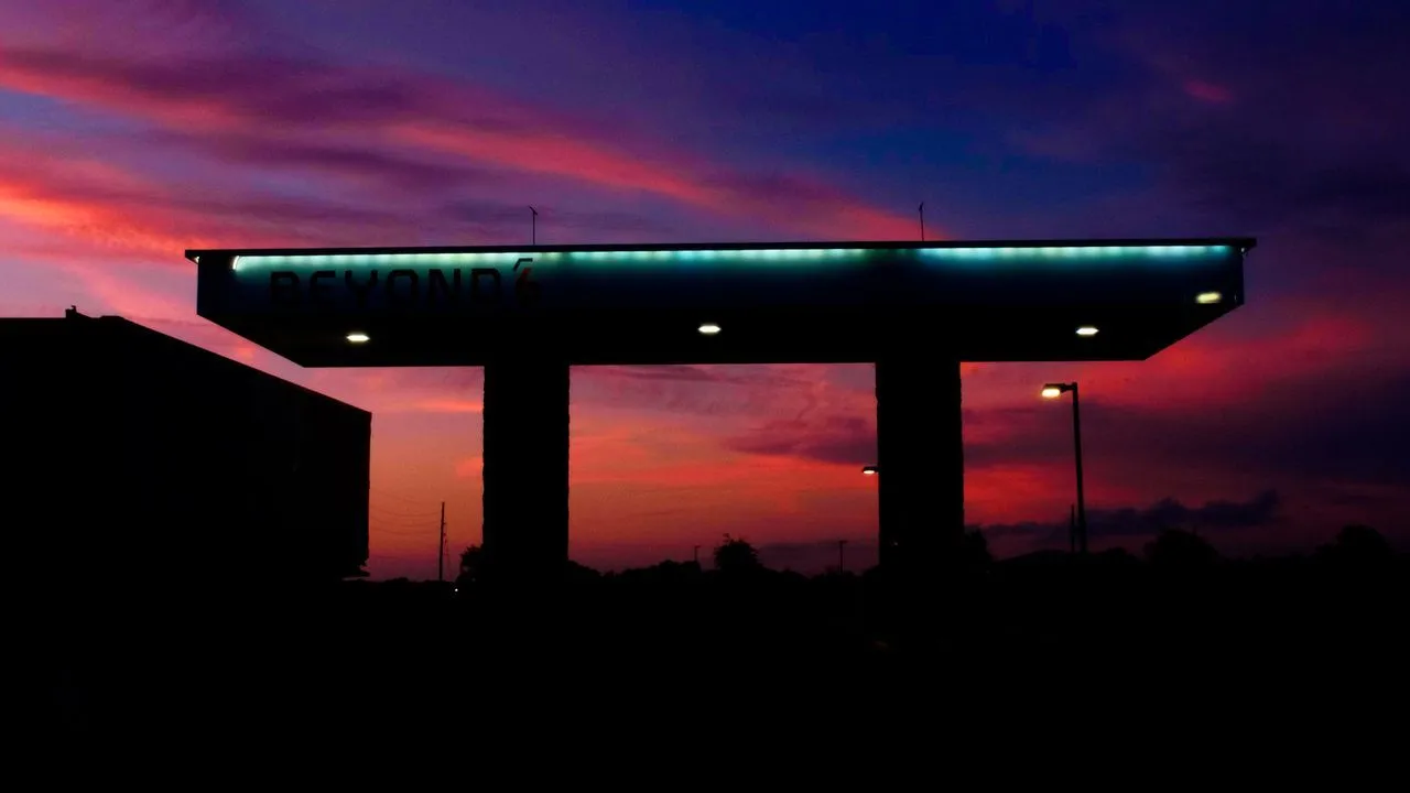 Illuminated roadside canopy beneath a vivid red and blue sunset.